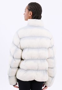 Puffjacka i krämfärg med grå accenter, med hög krage, kviltad textur och oversized siluett. Vinklade sömmar betonar formen.