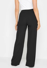 Zwarte, wijde broek van een zachte, rekbare stof. Heeft een elastische tailleband en een gladde textuur, geschikt voor casual wear.