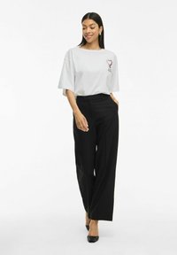 Lichtgrijze, loszittende T-shirt met een grafisch ontwerp op de borst. Gecombineerd met hoge zwarte wijde broek en zwarte hakken.