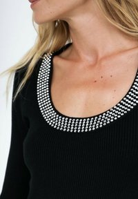 Top noir côtelé avec un décolleté légèrement arrondi orné de strass argentés. La texture est lisse, mettant en valeur les embellissements scintillants.