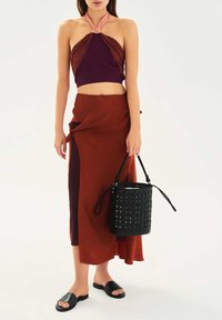 Top z vrvico za vrat v globoki vijolični in koralni barvi, kombiniran z rjavo zavito krilo. Črna tkana torbica v obliki vedra in črne natikače.