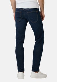 Ciemnoniebieskie dżinsy o slim fit, z kontrastowymi pomarańczowymi szwami i dwiema tylnymi kieszeniami. Zestawione z białymi sneakersami.