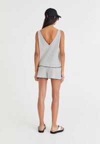 Canottiera a righe con profondo scollo a V sul retro, abbinata a pantaloni corti coordinati. Il tessuto è leggero e presenta un orlo a forma di onda. Cappellino nero e sandali.