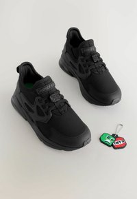 Baskets noires avec une tige en tissu texturé, dotées d'un système de laçage proéminent, d'un bout rond et d'un accessoire de porte-clés détachable.