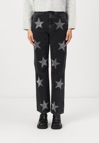 Svart jeans med sølvstjernepynt, rett ben-design, høy midje og lommer, brukt med svarte sko og en lys grå genser.