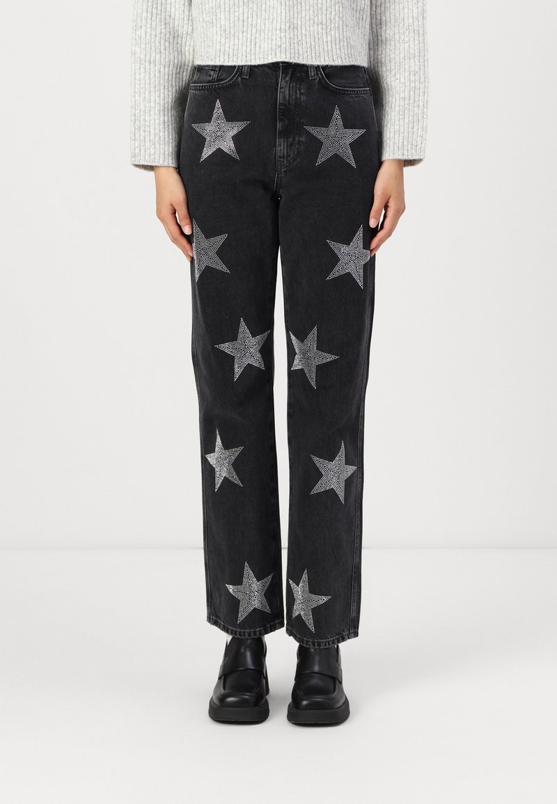Svart jeans med sølvstjernepynt, rett ben-design, høy midje og lommer, brukt med svarte sko og en lys grå genser.