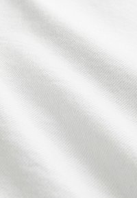 Gros plan sur un tissu blanc montrant une texture tissée fine et des plis doux créant de légères ombres.