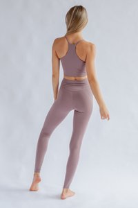 Sporta komplekts mierīgā mauve krāsā, kas ietver pieguļošu racerback topu un augstās jostas bikses. Gluda tekstūra ar elastību komfortam un kustībai.