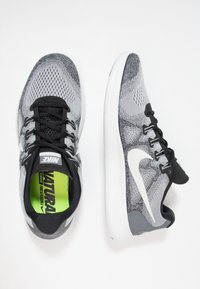 Scarpe da corsa Nike grigie e nere con logo Swoosh bianco, lacci neri e solette verdi brillanti con la scritta "CORSO NATURALE libero e flessibile."