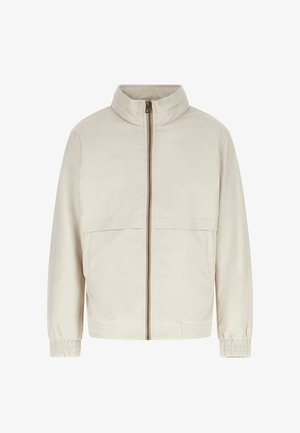 Beežist hele lukuga jope kõrge krae, pikkade varrukate, elastsete mansettide ja küljetaskutega, valgel taustal.