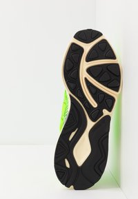 Grüne Sportschuhsohle mit einer strukturierten schwarzen Gummiaußensohle und einer neutralen Zwischensohle, die ein auffälliges Profilmuster zeigt.