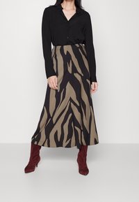 Schwarzes Langarmshirt und einen Midirock mit einem Zebrastreifenmuster in Beige und Dunkelbraun. Burgunderfarbene Absatzstiefel runden das Outfit ab. Glatte Stofftextur.