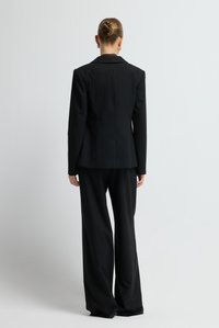 Zwart op maat gemaakt pak met een blazer en brede pijpen. De blazer heeft een reverskraag en een getailleerd ontwerp. Gladde textuur.