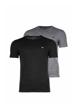 Giovane uomo con capelli corti che indossa una t-shirt nera semplice a maniche corte con un piccolo logo bianco sul petto e pantaloni blu.