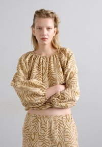 Beige Gemusterte Bluse mit weiten Ärmeln und elastischem Kragen, kombiniert mit passenden Shorts mit elastischem Bund. Mit einem wellenförmigen, abstrakten Design.