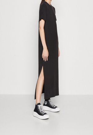 Robe noire, mi-longue, avec des manches courtes et des fentes latérales. Portée avec des baskets montantes noires dotées d'une semelle blanche. Design simple, texture douce.