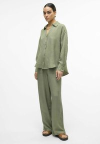 Completo coordinato in verde oliva composto da camicia e pantaloni a gamba larga; tessuto leggero e testurizzato, colletto, chiusura con bottoni e tasche frontali sui pantaloni.