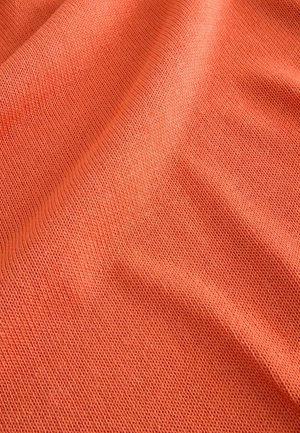 Coral-colored knitted fabric with a textured, open weave. The material appears soft and drapes gently, showcasing subtle ripples.