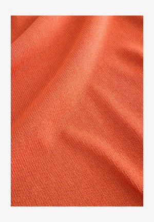 Koralfarvet strikket stof med en struktureret, åben vævning. Materialet ser blødt ud og falder let, hvilket fremhæver subtile bølger.