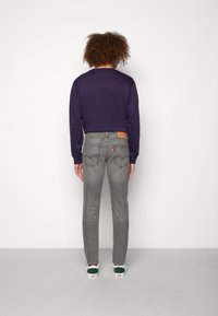 Fialová dlouhá košile, šedé slim-fit džíny s kapsami vzadu a tenisky s zelenými akcenty. Jednoduchý, každodenní outfit s minimálními vzory.
