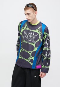 Μακρυμάνικη φούτερ με σκούρη μωβ βάση και πράσινα αφηρημένα μοτίβα, γαλάζια ένθετα στους ώμους και γραφικό λογότυπο στο μπροστινό μέρος.