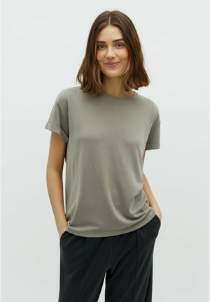 T-shirt s kratkim rukavima i okruglim izrezom u prigušenoj maslinastoj boji, izrađen od mekog materijala s opuštenim krojem, uparen s klasičnim tamnim hlačama.