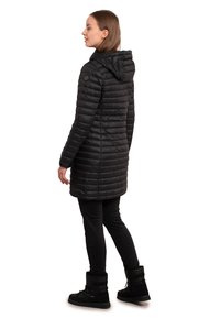 Zwarte pufferjas met een kap, doorgestikt ontwerp en lange lengte. Gemaakt in combinatie met zwarte leggings en winterlaarzen, wat een strakke, gestroomlijnde uitstraling toont.