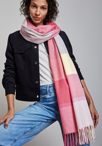 Strickschal mit einem Farbverlauf aus pink, flieder und cremefarbenen Streifen, mit Fransen. Kombiniert mit einer schwarzen Jacke und blauen Jeans.