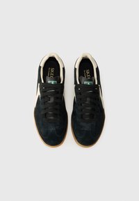 Black suede sneakers with a cream tongue and accents, featuring black laces, a gum rubber sole, and a logo tag visible on the tongue.
