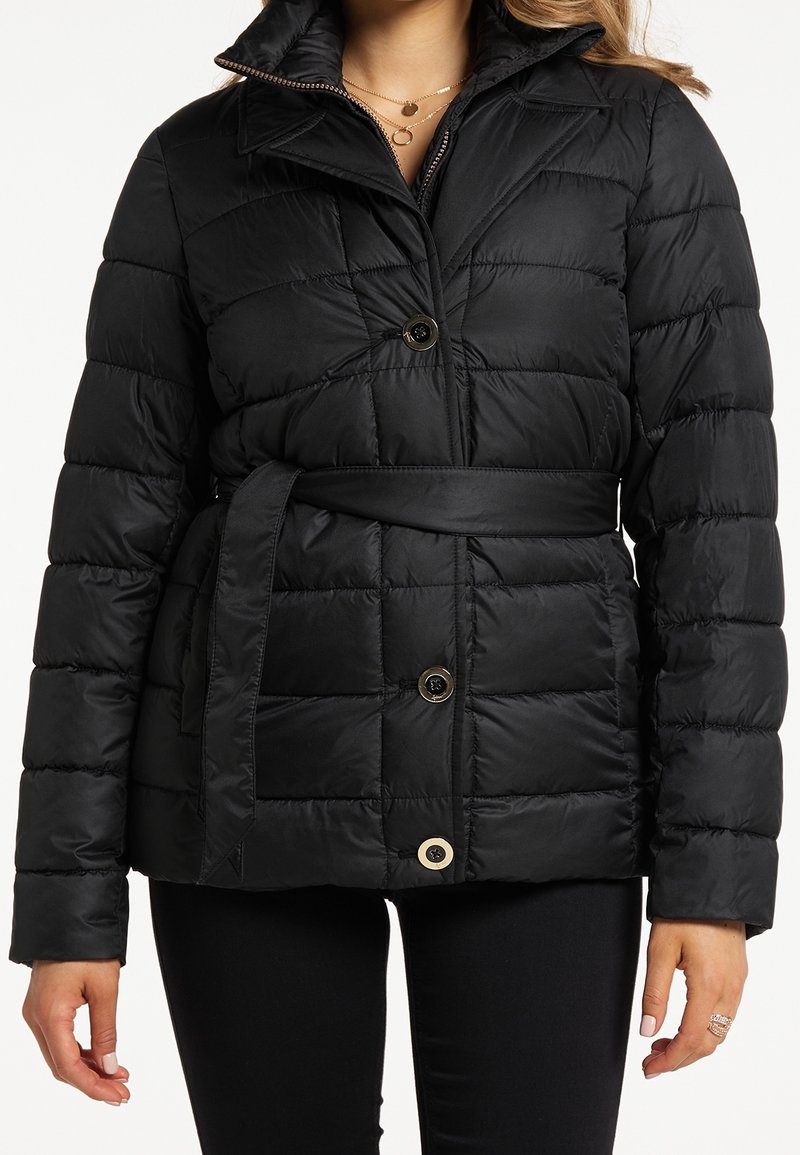 Chaqueta acolchada negra con cintura ceñida, que presenta un patrón de acolchado, cuello elevado y grandes botones. Textura de tela lisa y brillante.