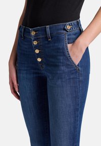 Jeans in denim di colore blu scuro con vita alta, chiusura a cinque bottoni dorati, tasche frontali e un design slim fit.