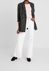 Blazer a quadri bianco e nero sopra una maglietta rosa chiaro, abbinato a jeans bianchi a gamba larga e scarpe nere a punta con finitura textured.
