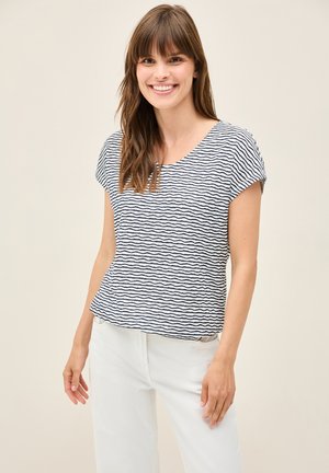 Blusa de manga corta en patrón de olas azul marino y blanco, confeccionada en tejido ligero; escote redondeado y corte holgado, combinada con pantalones blancos.