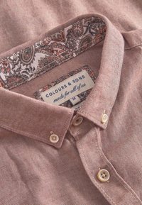 Camicia button-up rosa chiaro con una texture a strisce, dotata di fodera del colletto a fantasia e due chiusure a bottone sul davanti.