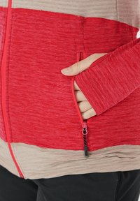 Röd och beige zip-up jacka i texturerad tyg, med en kontrasterande dragkedja, sidofickor och långärmar med åtsittande manschetter.