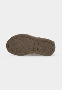 Semelle d'une chaussure marron avec une semelle texturée et un petit logo circulaire près du centre, affichée sur un fond clair uni.