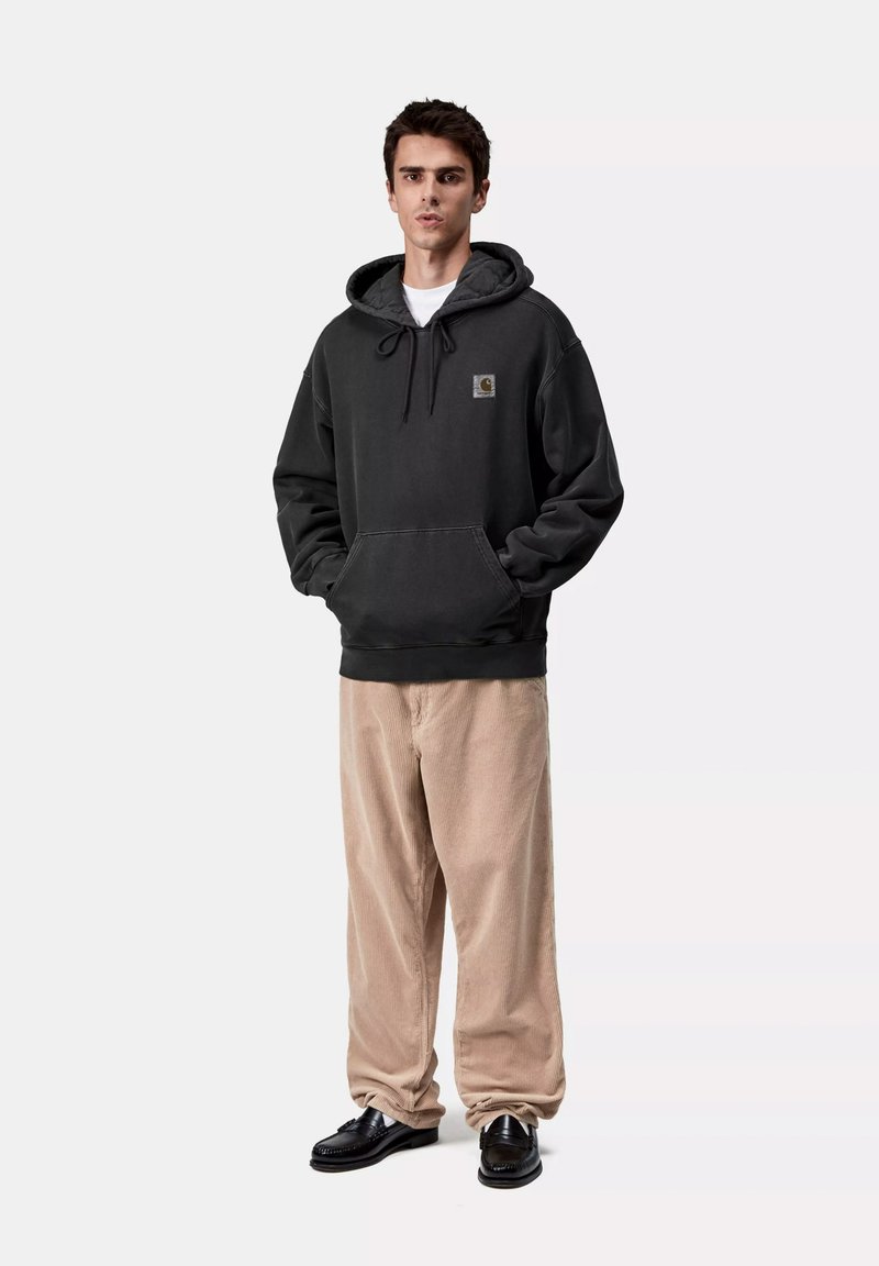 Sudadera gris oscura de tela suave, con un bolsillo delantero y capucha ajustable. Combinada con pantalones de pana beige y zapatos negros.