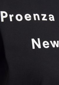 Svart t-shirt med vit tryckt text som säger "Proenza New", med en slät textur och figurnära design.