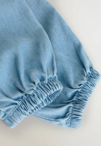 Hellblauer Denim-Stoff mit gerafften elastischen Bündchen, der eine weiche Textur und ein sauberes Finish aufweist und einen entspannten Stil zeigt.