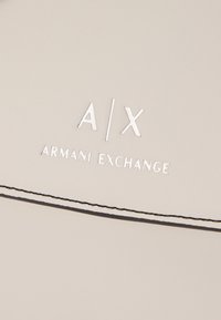 Pochette en simili cuir beige avec des coutures noires, arborant un logo argenté embossé "A/X ARMANI EXCHANGE" sur le devant.
