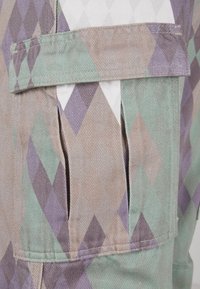 Multicolored diamond-patterned fabric features green, purple, and beige hues. Includes a side pocket with unfinished edges for a raw look.