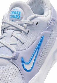 Nike barnskor i vitt med ljusblå detaljer. Har mesh-överdela, böjda spikar på sidorna och cirkulär logotyp på tungan.