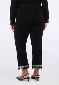 Černé kalhoty s těsně padnoucím pasem, zdobené texturovaným třásňovým lemem s stříbrnými detaily. Střih do délky kotníků, v kombinaci s podpatky.