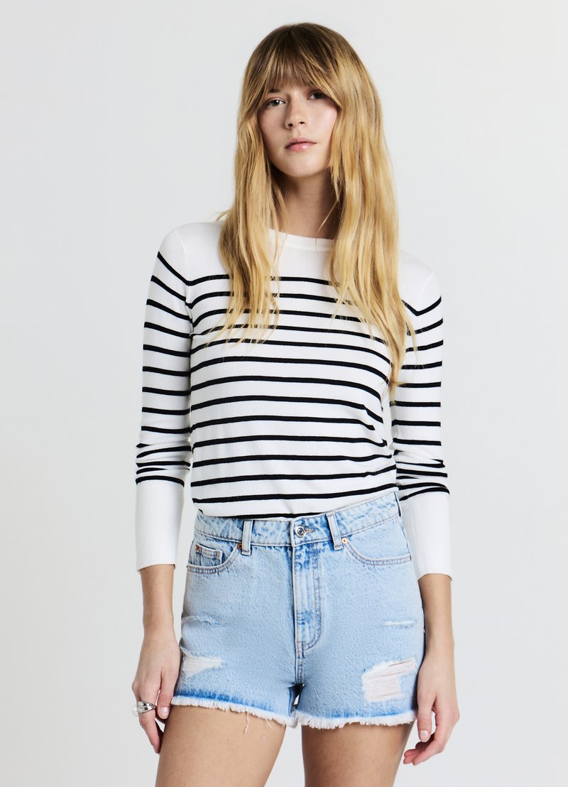 Haut à manches longues blanc avec des rayures horizontales noires, associé à un short en denim bleu clair avec des détails déchirés et un ourlet effiloché.