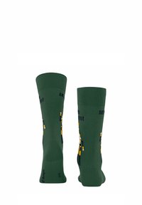 Zielone skarpetki z figlarnym wzorem z żółtymi postaciami. Materiał jest miękki, a przy mankiecie ma prążkowaną fakturę.