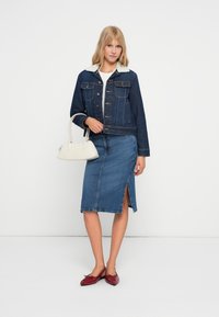 Denim jaka ar baltu vilnas apkakli, apvienota ar augsto vidukli denim svārkiem ar sānu šķēlumu. Aksesuāri ietver baltu rokassomu un sarkanas kurpes.