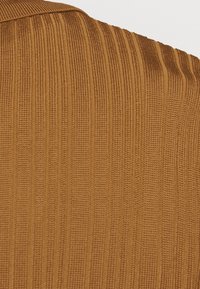 Tan ribbat tyg med vertikala ribbor, har en texturerad yta. Materialet verkar mjukt och sträcker sig något.