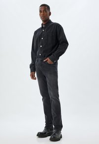 Camisa de mezclilla negra con botones y bolsillo en el pecho, combinada con jeans oscuros y botas de tobillo negras. Textura suave y diseño ajustado.