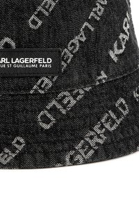 Zwarte denim emmerhoed met witte herhalende tekst en een rechthoekig label met "KARL LAGERFELD" in zwart reliëf.