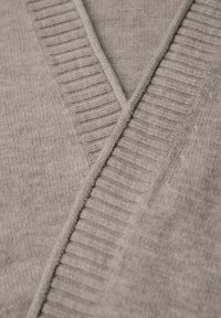 Ljusgrå tröja med V-halsdesign. Har ribbade detaljer längs halsringningen och en textur som kontrasterar mellan släta och stickade ytor.